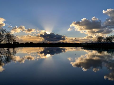 Wolkenlucht reflecteert in het water van IJsbaan / Jan Gorter